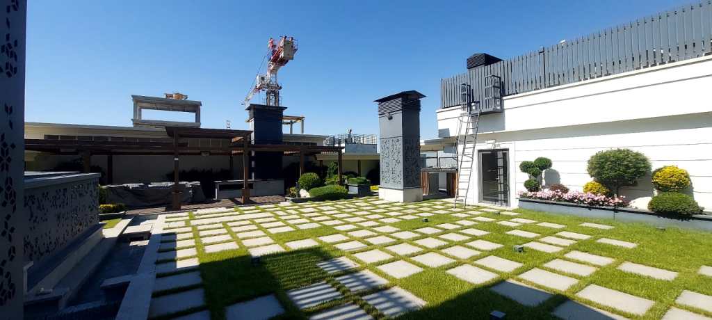 A modern roof garden space featuring a well-maintained lawn, stone pathways, and neatly arranged greenery. 