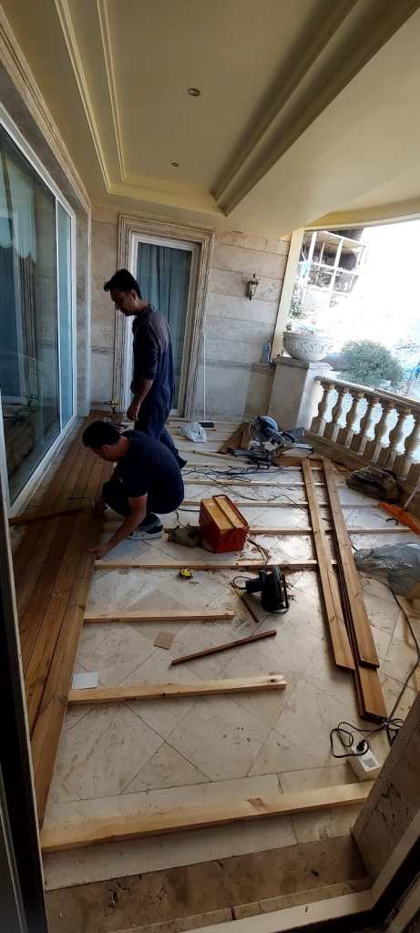 Workers installing wooden flooring during a balcony renovation project, showing the transformation process