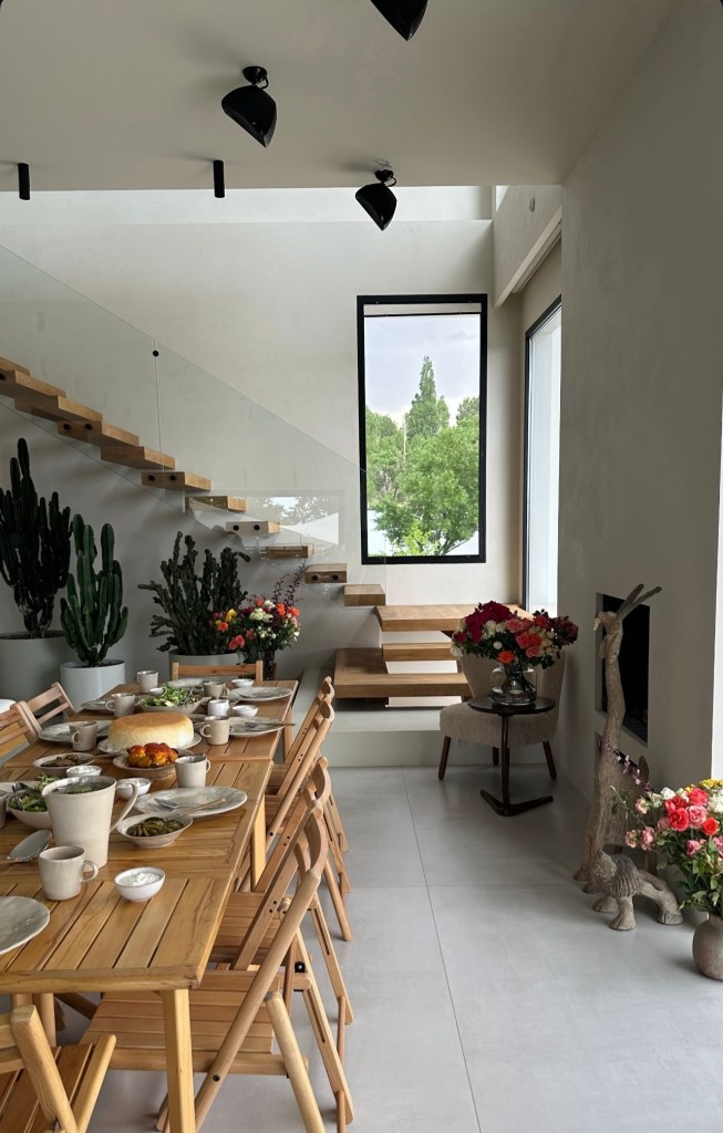 Contemporary wooden staircase integrated into a dining area, featuring natural light, plants, and a cozy interior renovation.