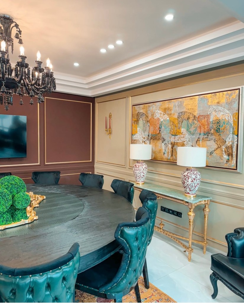Luxury dining room with round wooden table, green velvet chairs, chandelier, and wall art