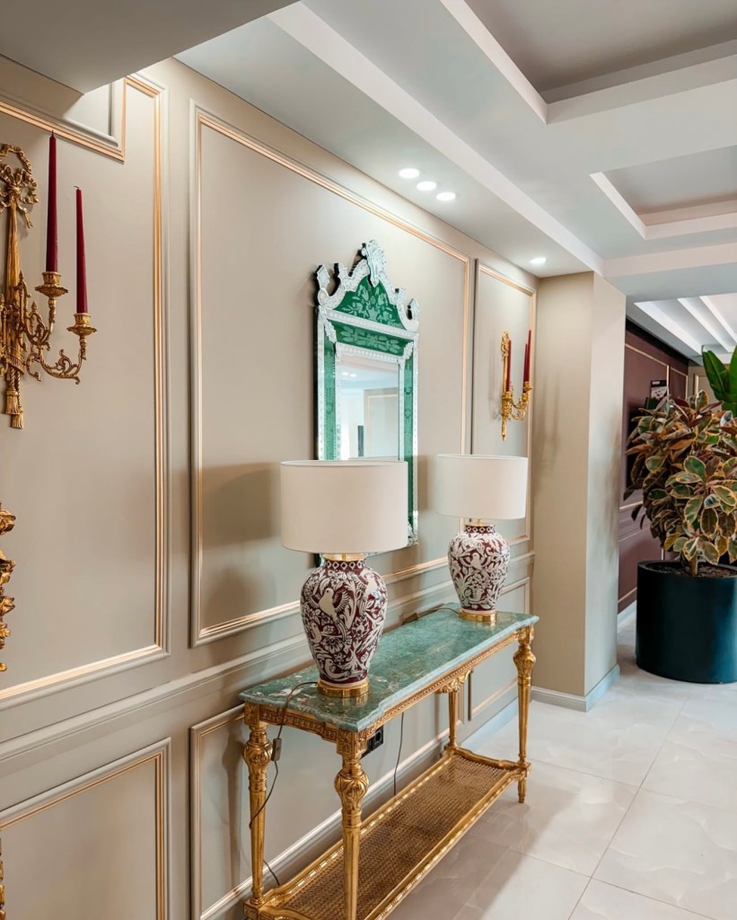 Elegant hallway interior with decorative mirror, classic green console table, and stylish wall lighting