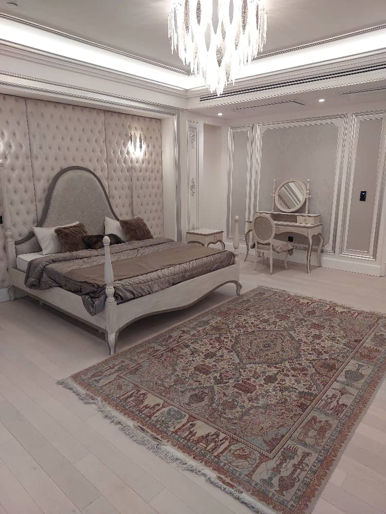 Luxury bedroom with upholstered headboard, classic vanity table, elegant chandelier, and Persian-style rug