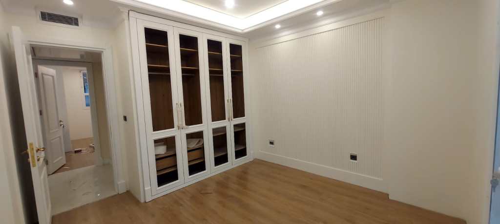 Modern bedroom with built-in white wardrobes, wooden flooring, and recessed ceiling lights