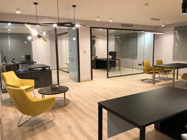 Modern office renovation with glass partitions, wooden flooring, and stylish yellow chairs creating a bright and professional workspace.